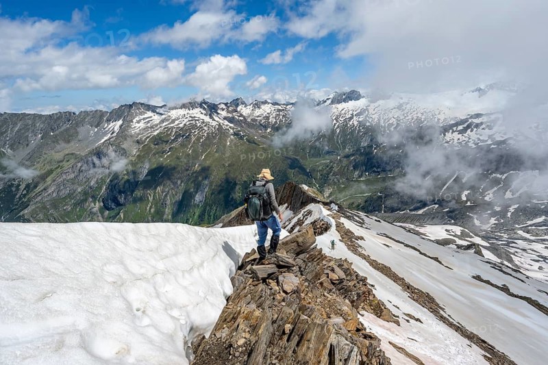 Mountaineer on a rocky ridge with snow, descent from the summit of Schönbichler Horn, view of snow-covered mountain peaks and valley Zemmgrund, Berliner Höhenweg, Zillertal Alps, Tyrol, Austria