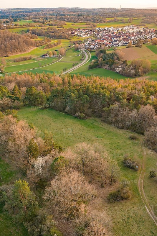 Broad landscape with meadows and forest surrounding a village and a curved road, e-bike tour, old sports field in Gechingen, Hecken and Gäu region, Calw district, Germany