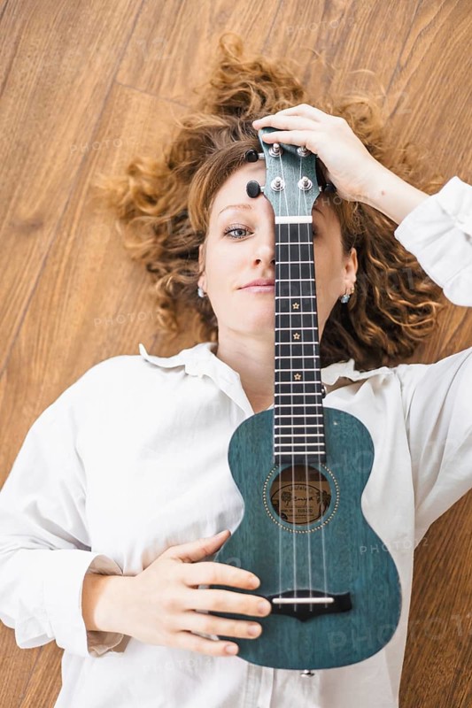A woman lies on the floor holding a blue ukulele, exuding a relaxed atmosphere