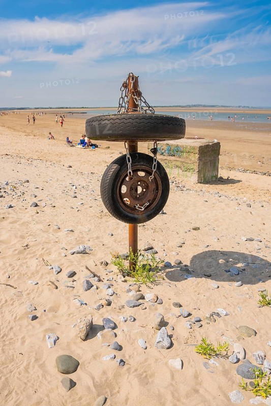 Old tires on posts as a sculptural element on sandy beach, blue sky, low tide, Howth beach, Ireland