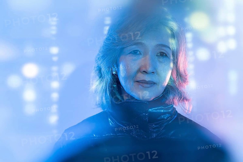 An elderly Asian woman is seen immersed in a futuristic digital environment, symbolizing the blend of tradition and technology in the metaverse. The blue lighting adds a modern touch
