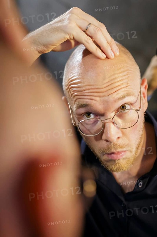 Symbolic photo on the subject of hair loss and baldness. A young man looks in the mirror for his hairline. Berlin, 13.08.2024