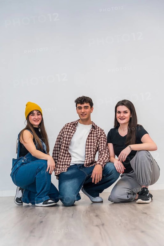 Three young dancers are kneeling in a dance studio, smiling and ready to start their lesson