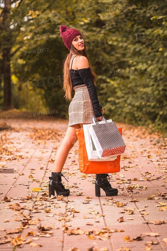 Portrait of a woman in autumn in a forest with brown leaves walking with paper bags after shopping