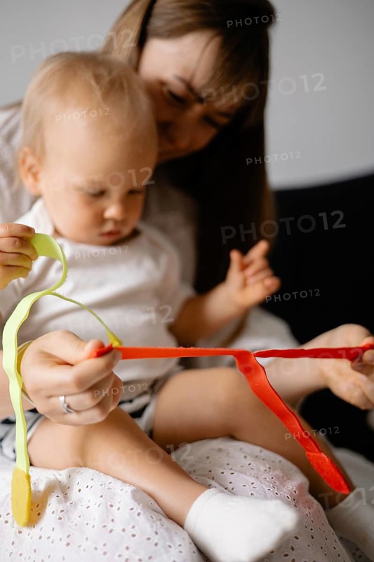 A woman and baby in white clothing play with colorful ribbons, creating an engaging and warm atmosphere