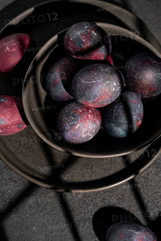 Top view of a ceramic bowl filled with dark, galaxy themed Easter eggs against dark background surface