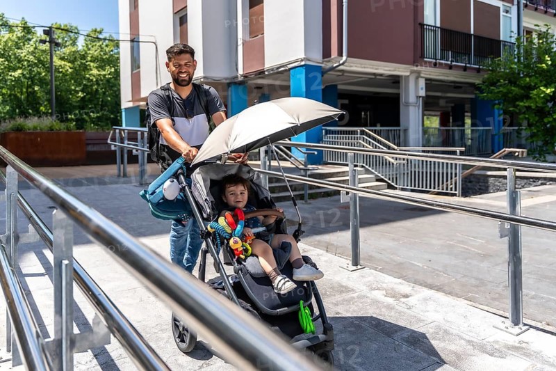 Father pushing a baby stroller with his happy son sitting inside, navigating an urban environment on a sunny day, showcasing family bonding and modern parenthood