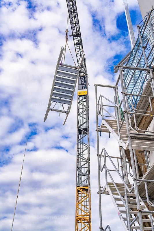 Crane lifts metal staircase into the air next to a scaffolding, in front of a cloudy sky, staircase extension to the new tower of the Calw central railway station on the new track of the Hermann Hessebahn, Calw, Black Forest, Germany