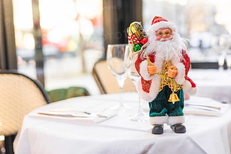 A festive table setting with a decorative Santa Claus figurine. The table is elegantly arranged with glassware and cutlery, creating a cheerful holiday atmosphere