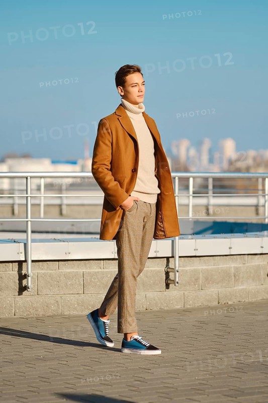 Spring, autumn outfit. Street fashion. Young man in checkered trousers, sweater and wool coat