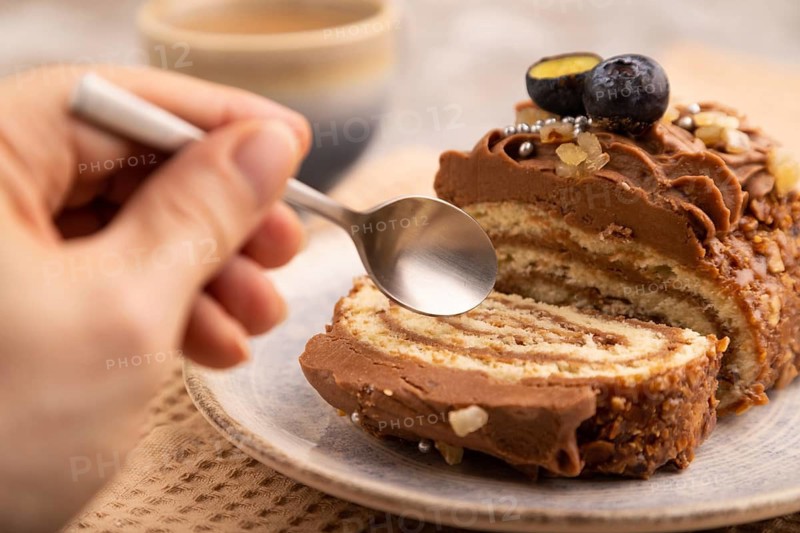 Sweet loaf with cream and carmel with hand, cup of coffee, on brown concrete background with linen beige textile, close up, side view, selective focus