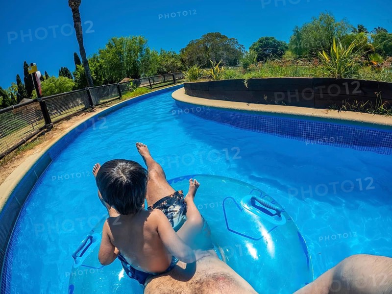 Father and son enjoying summer vacation, floating on inflatable ring in lazy river at water park