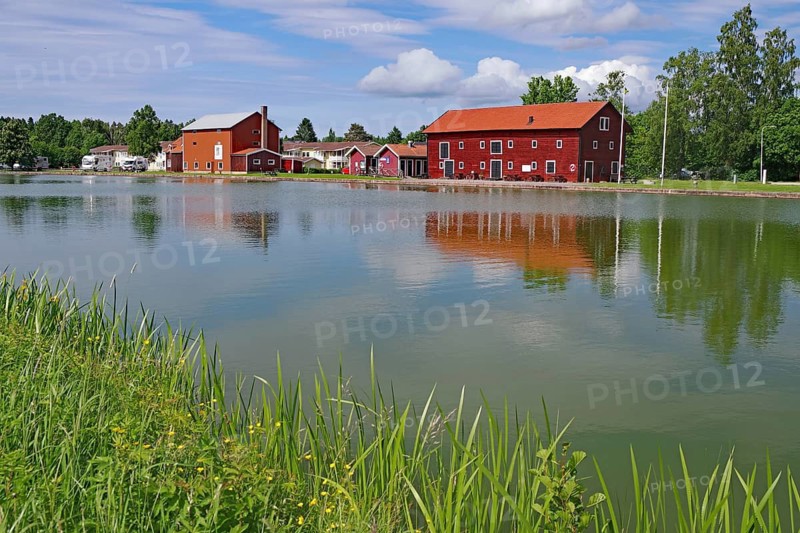 Red houses are reflected in calm water under a partly cloudy sky, Göta Canal, Götaleden, Västra Götalands län, Sweden