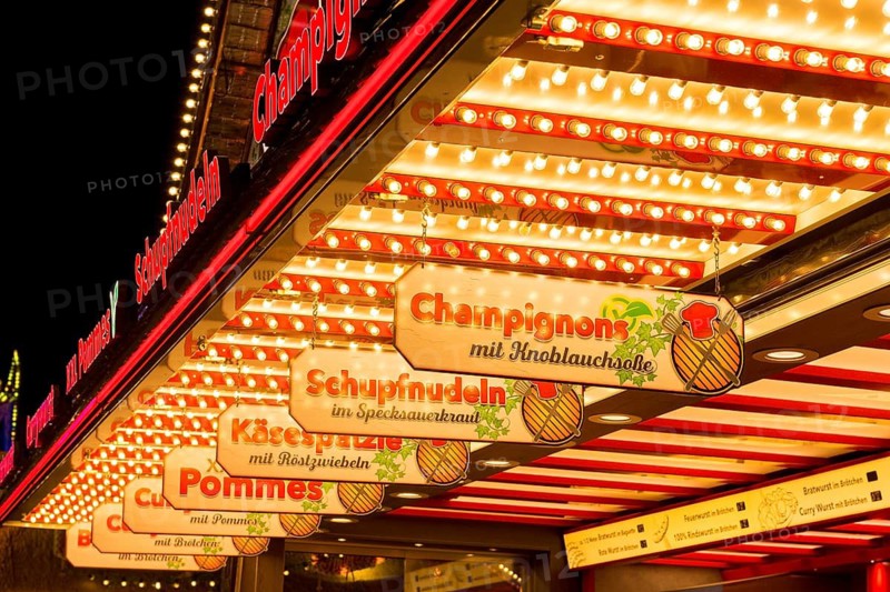 Illuminated market scene at night with signs for food: Mushrooms and cheese spaetzle, Cannstatter Wasen, folk festival, Bad Cannstatt, Stuttgart, Baden-Württemberg, Germany