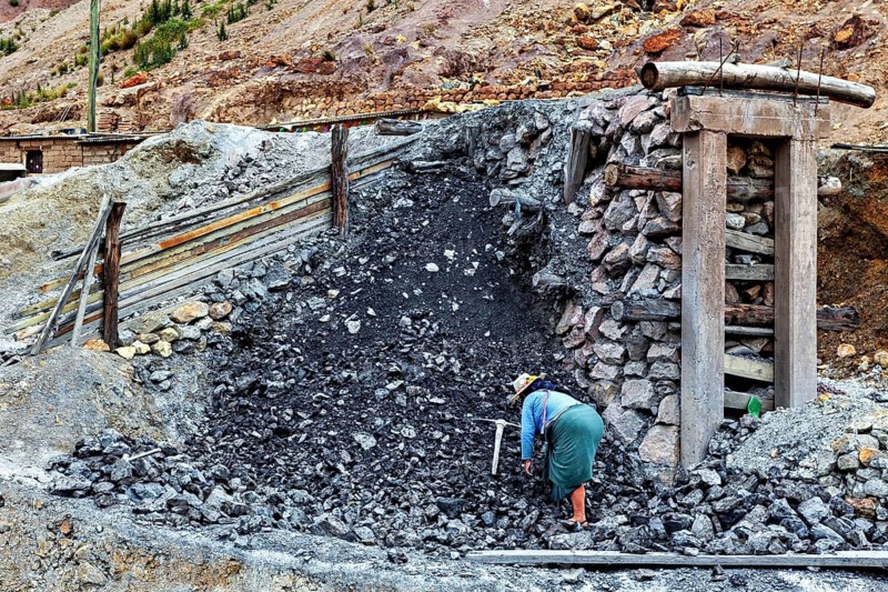 A worker with tools on a coal pile next to a stone structure, The Potosi Silver Mines on Cerro Rico in Bolivia