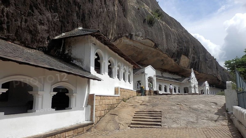Rock temple with white architecture under a large rock wall in daylight, Dambulla cave temple, Sri Lanka