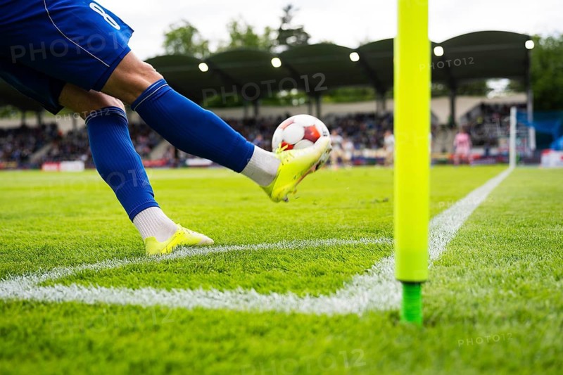 Football player taking a corner kick during a soccer match, striking the ball beside the corner flag on a green pitch in Legnica, Poland