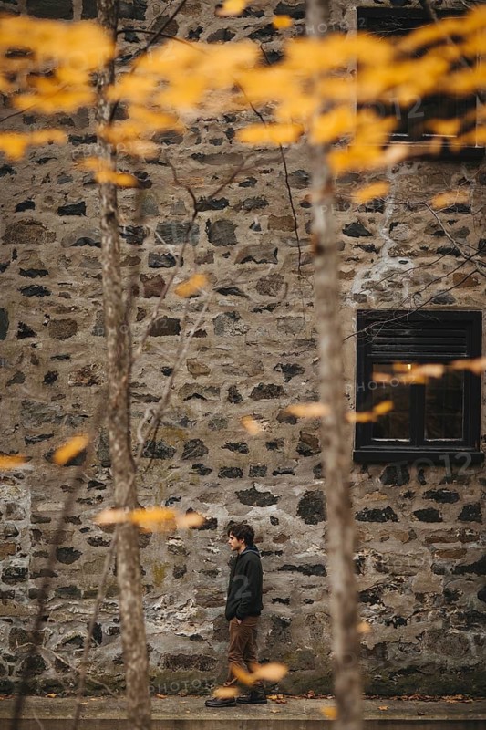 A person walks alongside a rustic stone building, surrounded by the warm hues of autumn leaves in Quebec, Canada. The scene captures the essence of a tranquil fall day