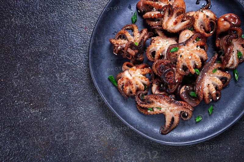 Grilled baby octopus, served with chopsticks, on a black plate, homemade, no people
