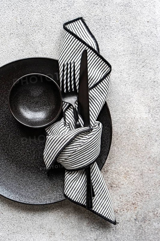 A minimalist black and white table setting featuring a sleek black plate, bowl, and cutlery, complemented by a folded striped napkin. Perfect for elegant dining themes