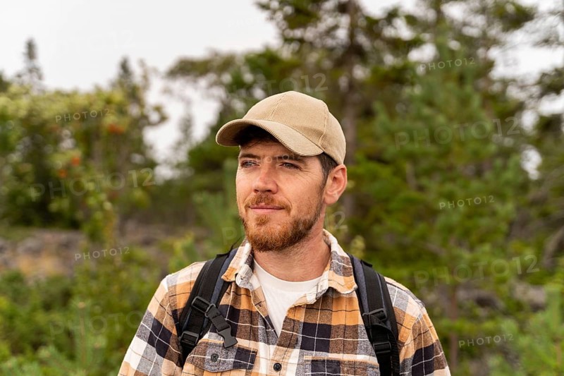 A man wearing a beige cap and plaid shirt explores the lush forests of Sweden. Capturing the spirit of adventure and outdoor exploration in a scenic natural setting
