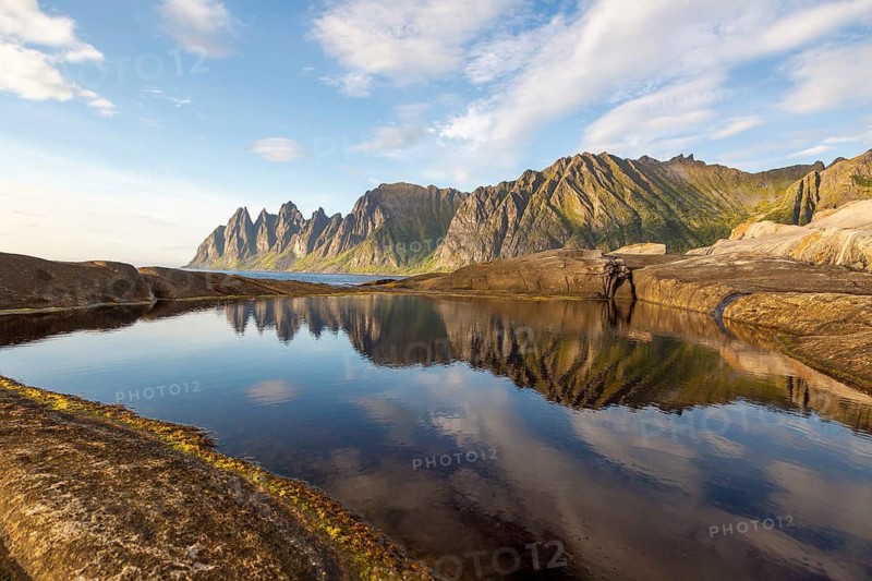 Crystal-clear reflection of the Okshornan mountain range in a large tide pool near Tungeneset, Senja, Norway