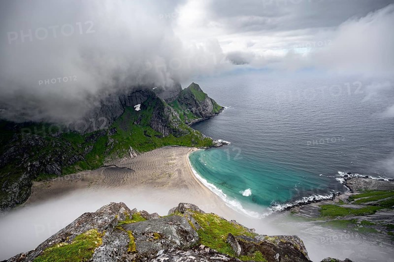 View from Helvetestinden summit, Bunesstranden sandy beach and blue sea, dramatic cloudy sky, Lofoten, Norway