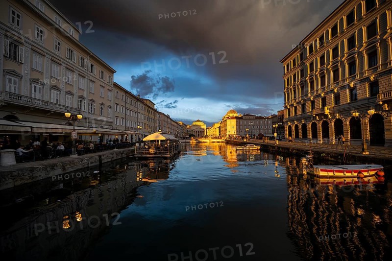 Grand Canal with boats and restaurants, Sant'Antonio Taumaturgo church reflected in the canal, in the evening light at sunset, dramatic clouds and atmospheric lighting, Trieste, Friuli-Venezia Giulia region, Italy
