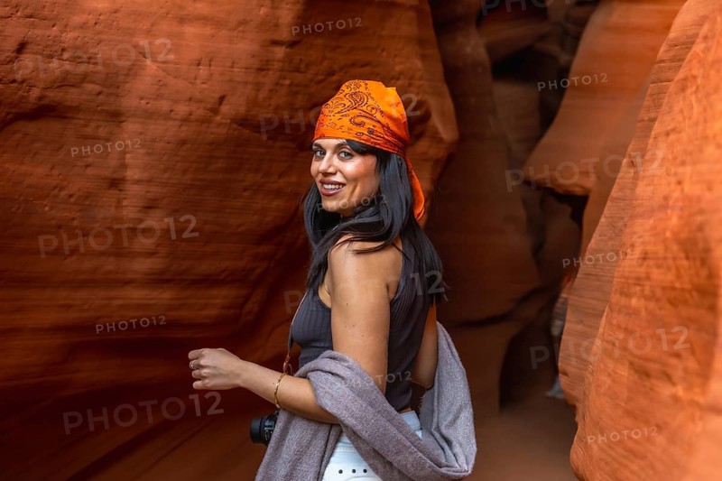 Woman tourist smiling and looking back while exploring wavy red sandstone formations and light patterns inside antelope canyon near page, arizona, enjoying the desert canyon scenery