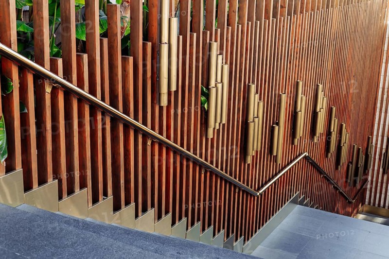 A beautifully crafted wooden stairway features vertical wooden slats and golden accents, surrounded by lush greenery. This architectural element showcases modern design in a city environment