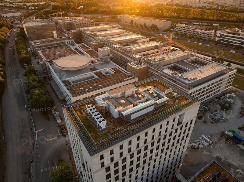 Large building complex at sunset with green roofs and urban surroundings, construction site of the new airfield clinic, Böblingen, Germany