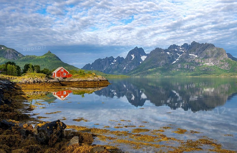 Red fishing hut on the shore, Rorbuer hut, picturesque fjord landscape at Raftsund fjord, mountains reflected in water, Vesterålen, Norway