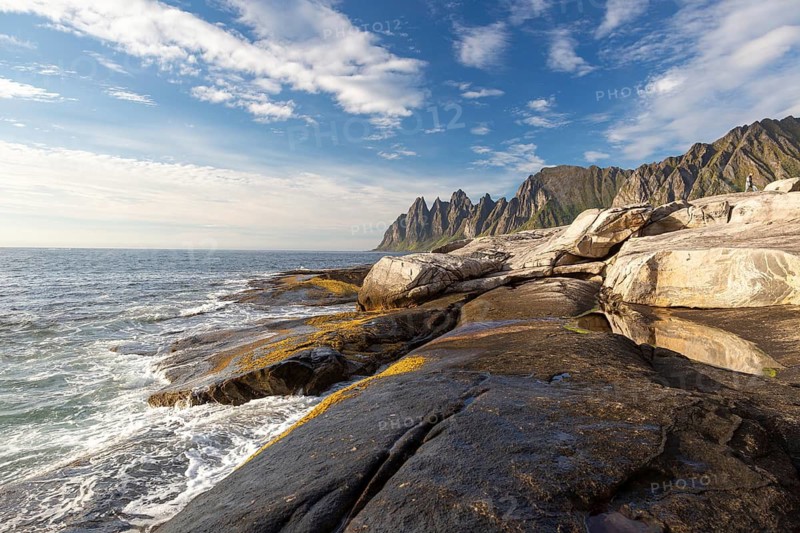 Waves hit the wet rocks of Tungeneset with the Okshornan Mountains in the background, Senja, Norway
