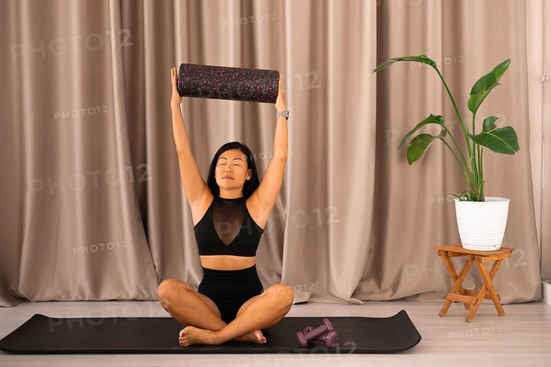 Woman lifts a foam roller during yoga session, showcasing balance and concentration