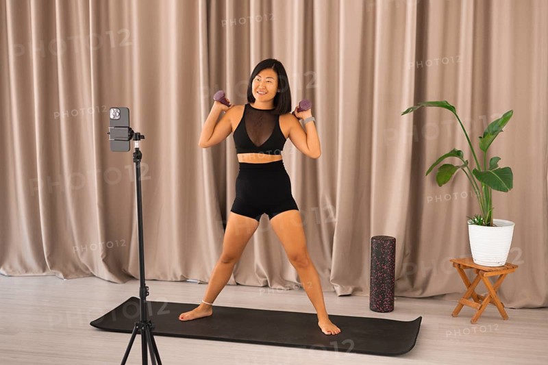 She is standing on a yoga mat with dumbbells, ready for a workout session