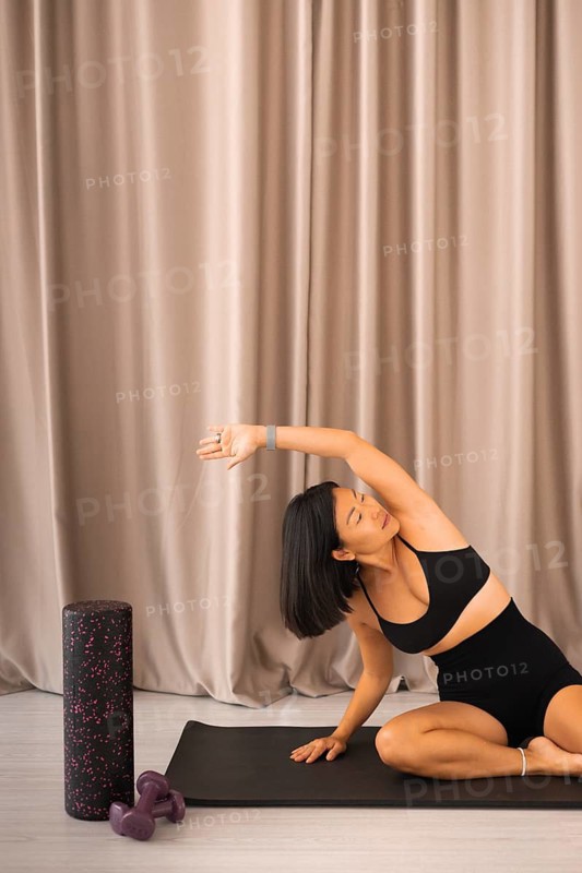 Woman stretching on a mat next to a foam roller in a serene setting