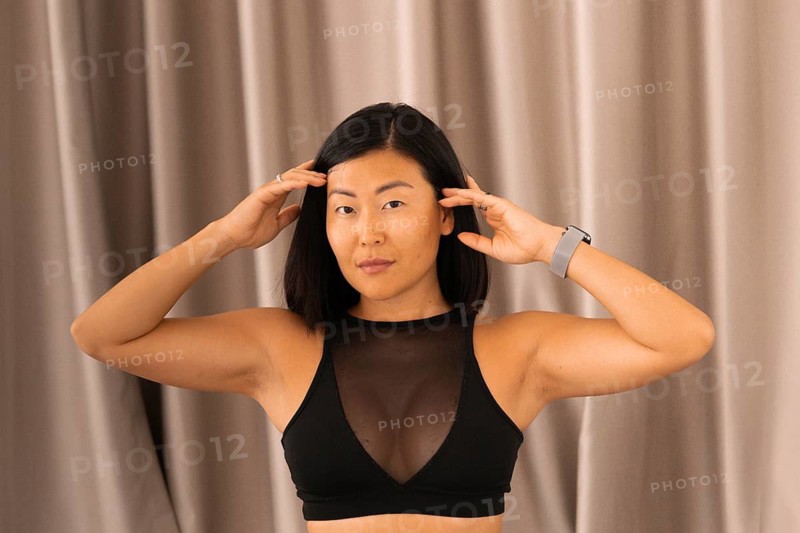 Close-up of a woman in a black top, focused and posing with hands near her face