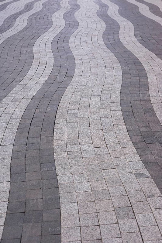 Curved lines of gray and white paving stones create an eye-catching pattern on an urban walkway. This modern design offers visual interest and enhances the pedestrian experience in the area