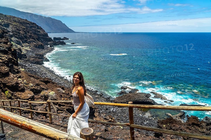 Woman standing on a wooden path along the rugged volcanic coastline of el hierro, immersing herself in the beautiful natural scenery and enjoying a relaxing vacation under the bright sunny sky