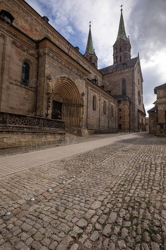20 August 2026, View of the historic Bamberg Cathedral with its stone facade and spires along a cobbled street in Bamberg, Germany