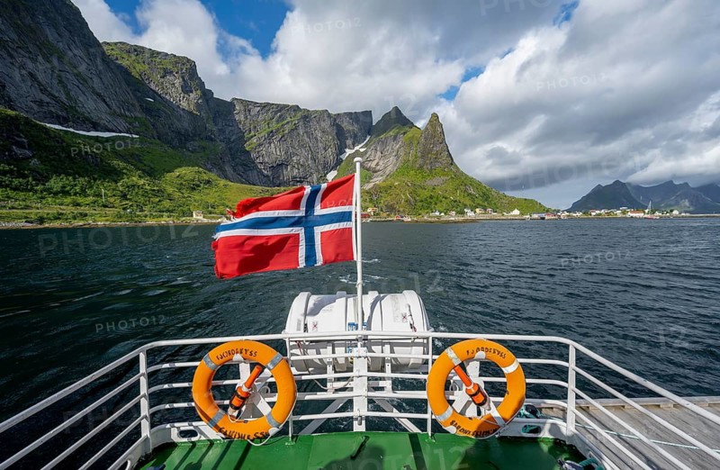 Boat trip on Reinefjord, Norwegian flag and fjord landscape with mountains, Lofoten, Norway