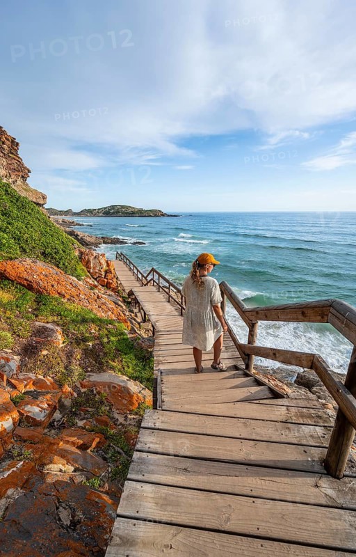 Young pretty woman wearing dress off coast and sea at Robberg Nature Reserve, Plettenberg Bay, South Africa