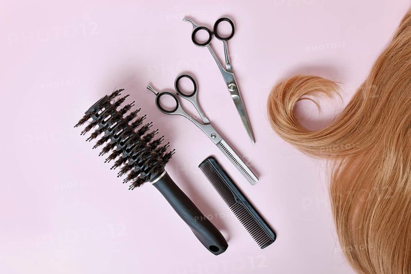 Flatlay of blonde hair with hair scissors, thinning scissors, comb and round brush