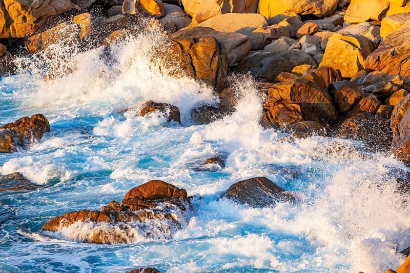 Surf at the coastline, blue water flows around the stones at Costa Paradiso in eveneing light, Sardinia, Italy