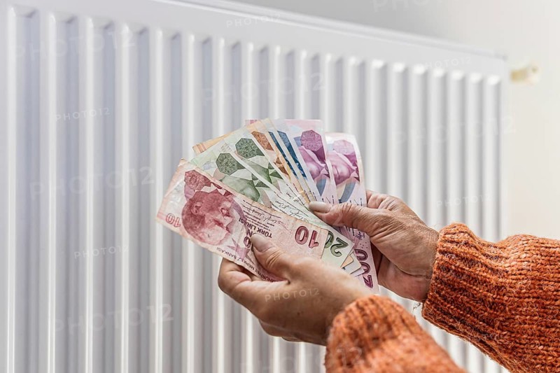 Woman holding Turkish lira banknotes near home radiator during winter heating season. Concept of increasing household heating expenses, inflation, rising energy prices, utility bills, cost of living