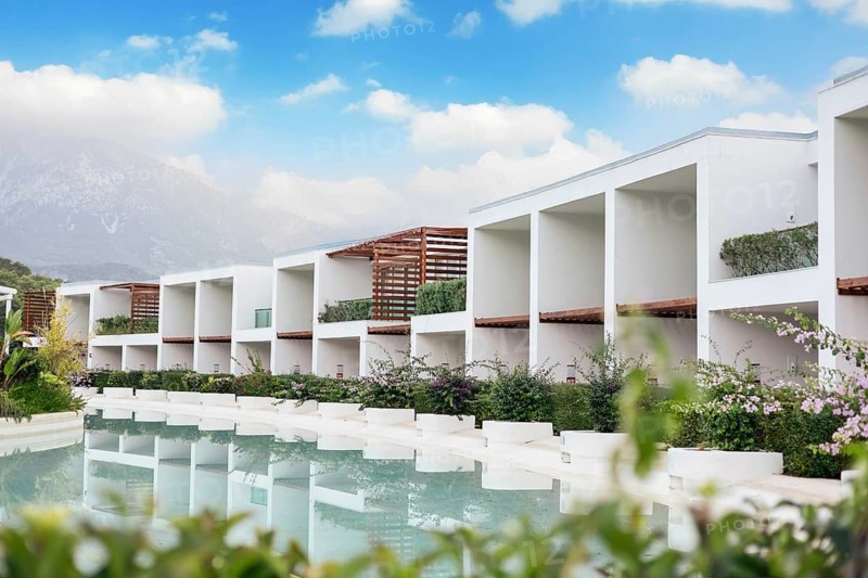 Modern white resort buildings hotel beside a tranquil pool, surrounded by greenery and under a blue sky with clouds during summer season. Antalya, Turkiye