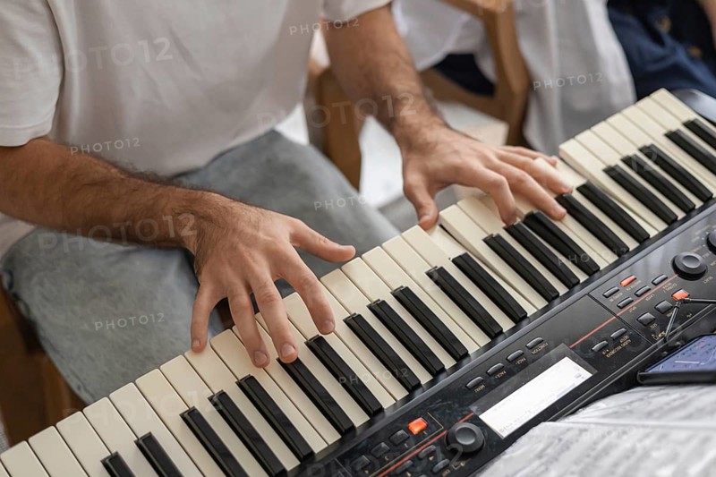 A close-up of a mans hands playing a keyboard in a cozy home setting. The atmosphere is relaxed and inviting, perfect for family music sessions