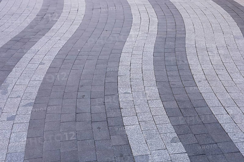 Curved lines of gray and white paving stones create an eye-catching pattern on an urban walkway. This modern design offers visual interest and enhances the pedestrian experience in the area