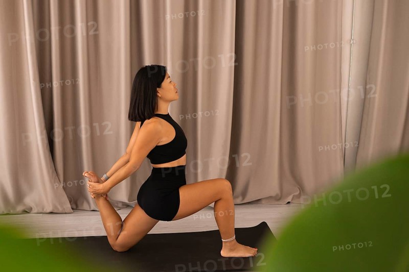 Yoga pose with woman on mat, curtains and plant adding focus and balance to the space