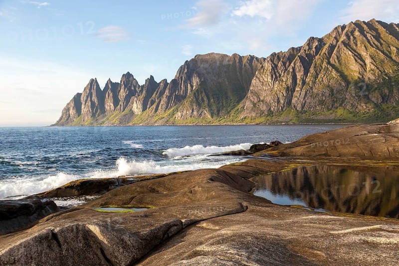 Ocean surf on the rocky coastline of Tungeneset with a view of the devil's teeth in sunlight, Senja Island, Norway
